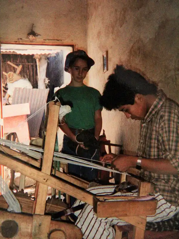 reine Baumwollstoffe In Guatemala beobachtet ein kleines Mädchen einen Handwerker beim Weben mit einem manuellen Webstuhl